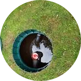 Open septic tank riser in a lawn, its green rim at ground level and the lid lifted off
